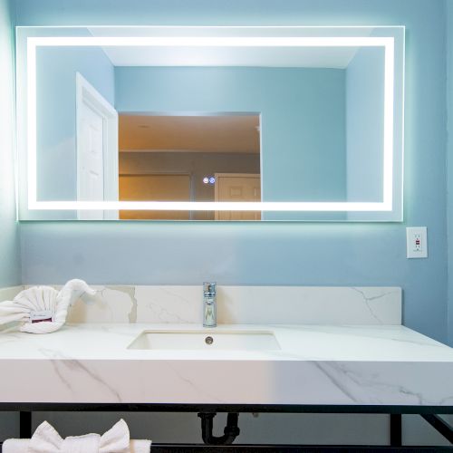 A bathroom with a marble sink, faucet, folded towel, and a large backlit mirror on a blue wall.