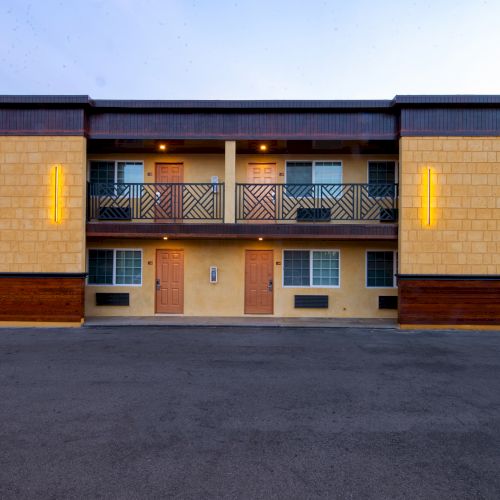 A modern two-story building with brown doors, windows, and illuminated yellow vertical lights on each side, set against a clear sky.