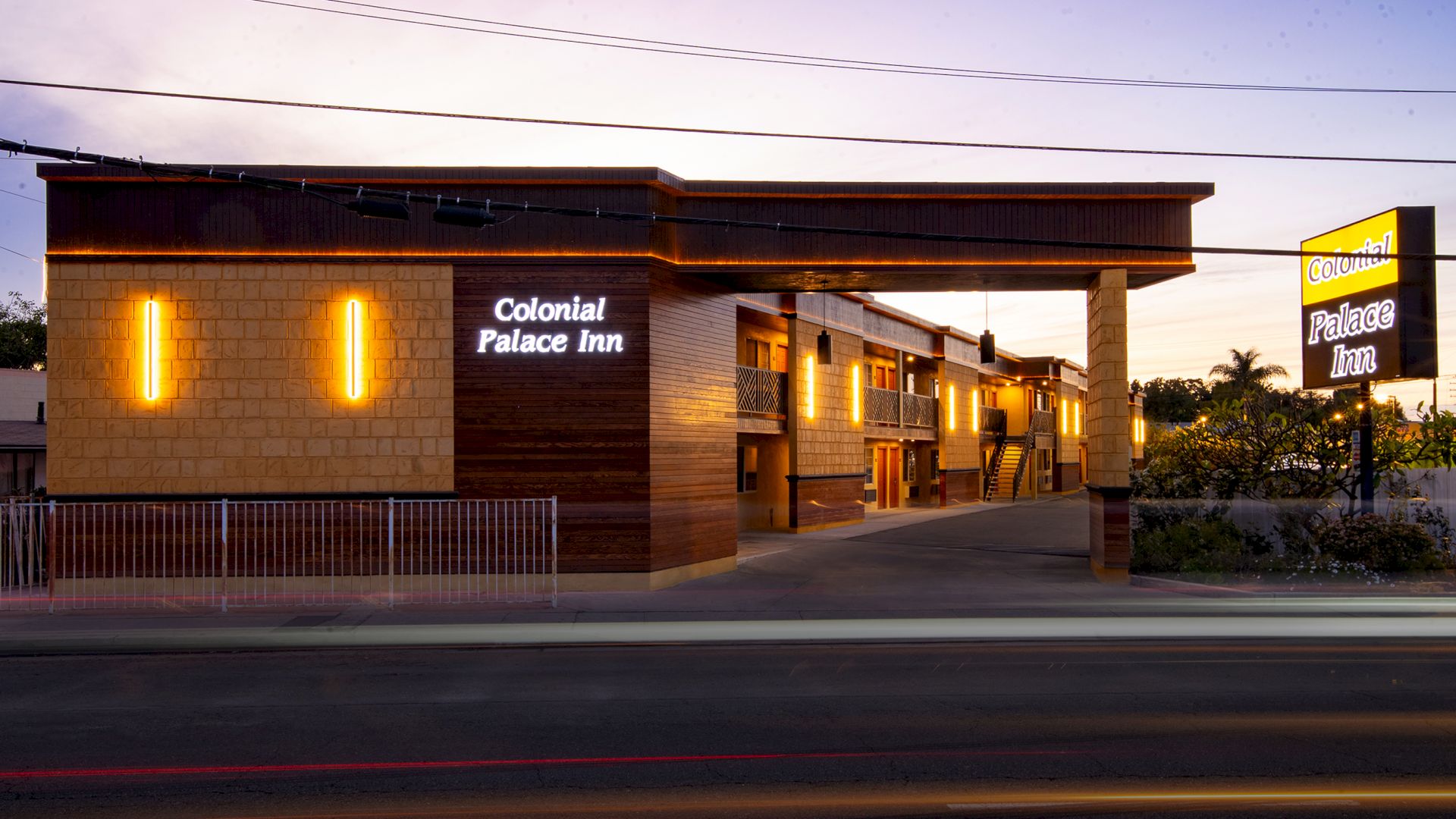 The image shows the exterior of the Colonial Palace Inn at dusk, with bright yellow and white lighting on the building.