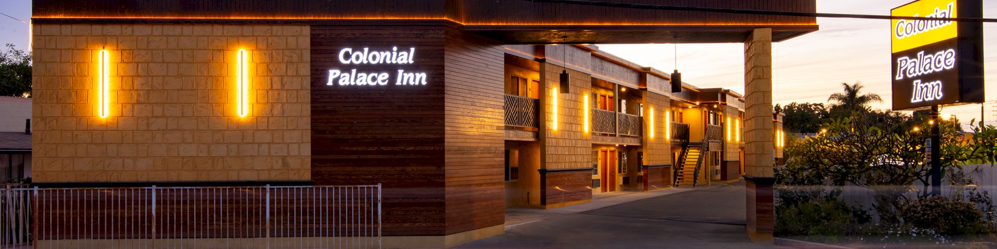 The image shows the exterior of the Colonial Palace Inn at dusk, with bright yellow and white lighting on the building.